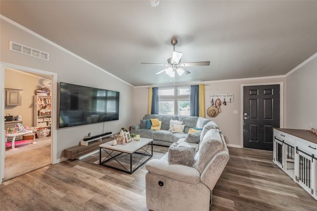 Living area featuring wood finished floors, crown molding, a ceiling fan, and lofted ceiling | Image 4