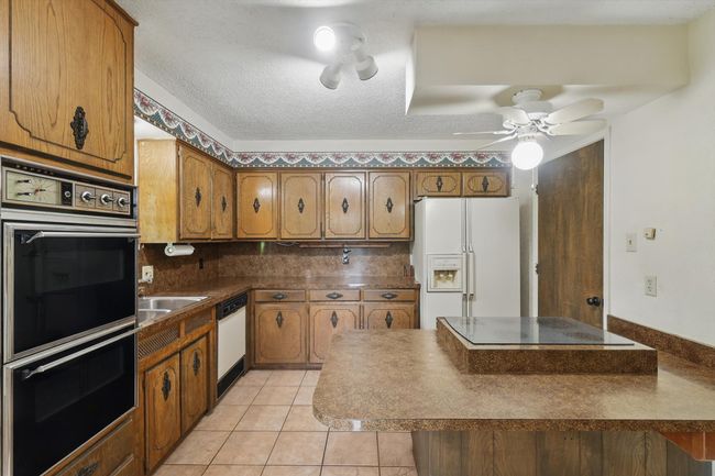 Kitchen with white appliances, brown cabinets, dark countertops, backsplash, and a ceiling fan | Image 17
