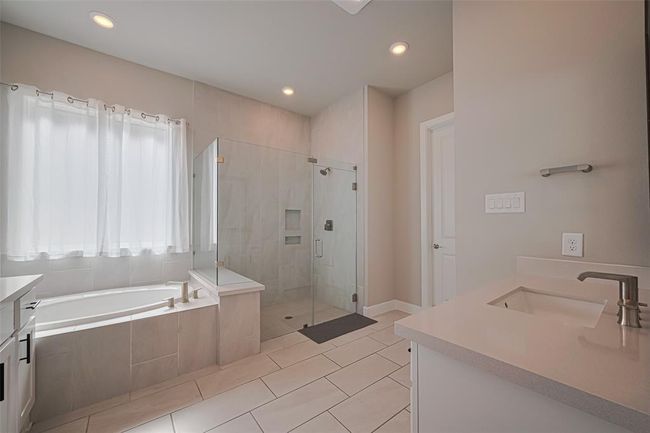 Primary bathroom features a spacious layout with a glass-enclosed shower, a large soaking tub, and a sleek vanity. Natural light fills the room through a window with sheer curtains, creating a bright and inviting space. | Image 22