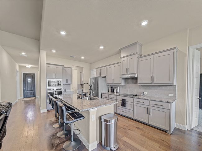 Kitchen with stainless steel appliances, gray cabinetry, a kitchen bar, tasteful backsplash, and recessed lighting | Image 10