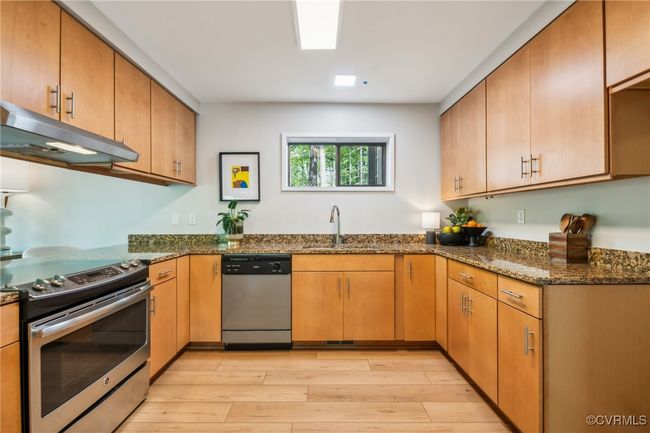 Kitchen featuring stainless steel appliances, light wood-style flooring, a sink, dark stone countertops, and under cabinet range hood | Image 28
