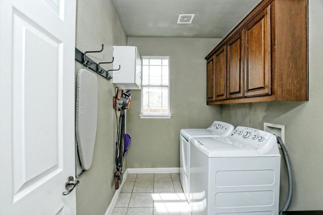 Clothes washing area with cabinet space, washing machine and clothes dryer, baseboards, and light tile patterned flooring | Image 13