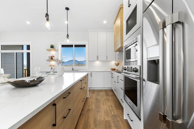 Kitchen with appliances with stainless steel finishes, wood finished floors, decorative light fixtures, recessed lighting, and white cabinetry | Image 7