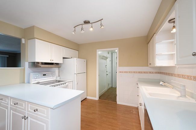 Kitchen with white appliances, range hood, white cabinets, open shelves, and tile walls | Image 14