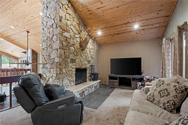 Carpeted living room with wooden ceiling, lofted ceiling, and a stone fireplace | Image 20
