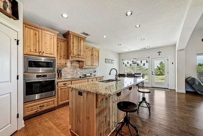 Kitchen featuring stainless steel appliances, a breakfast bar, light stone counters, decorative backsplash, and dark wood finished floors | Image 13