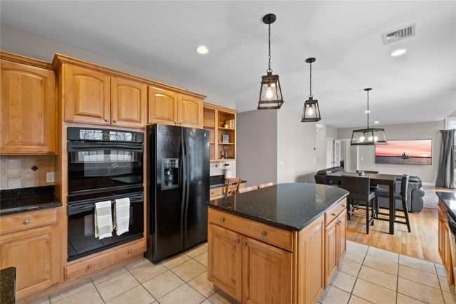 Kitchen with dark stone countertops, visible vents, black appliances, pendant lighting, and light tile patterned flooring | Image 13