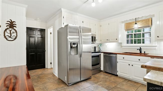 Kitchen with appliances with stainless steel finishes, decorative backsplash, stone finish floors, white cabinets, and crown molding | Image 44