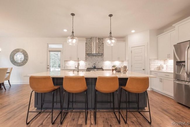 Kitchen featuring stainless steel refrigerator with ice dispenser, white cabinets, decorative backsplash, an island with sink, and recessed lighting | Image 34
