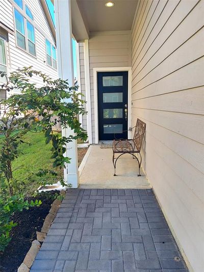 This is a welcoming entrance with a modern dark door, a paved walkway, complemented by a neatly landscaped area with shrubs. | Image 2