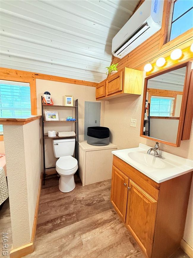 Bathroom featuring an AC wall unit, wood finished floors, vanity, electric panel, and toilet | Image 16