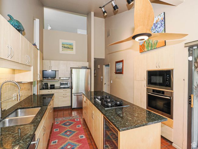 Kitchen featuring appliances with stainless steel finishes, dark tile patterned floors, wine cooler, a center island, and backsplash | Image 23
