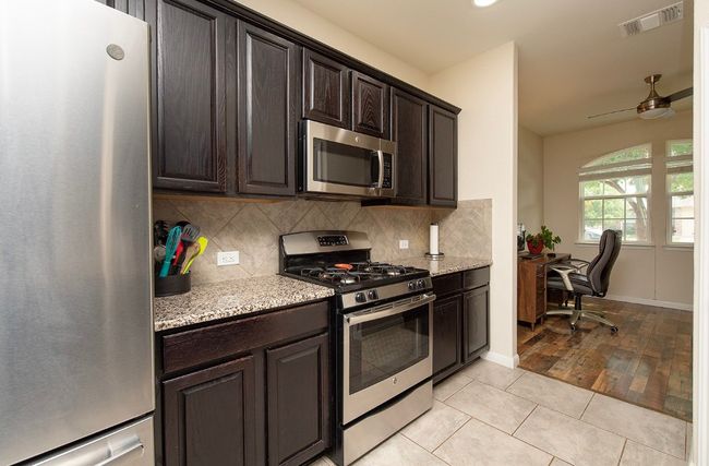 Kitchen featuring stainless steel appliances, a ceiling fan, backsplash, a desk, and recessed lighting | Image 7