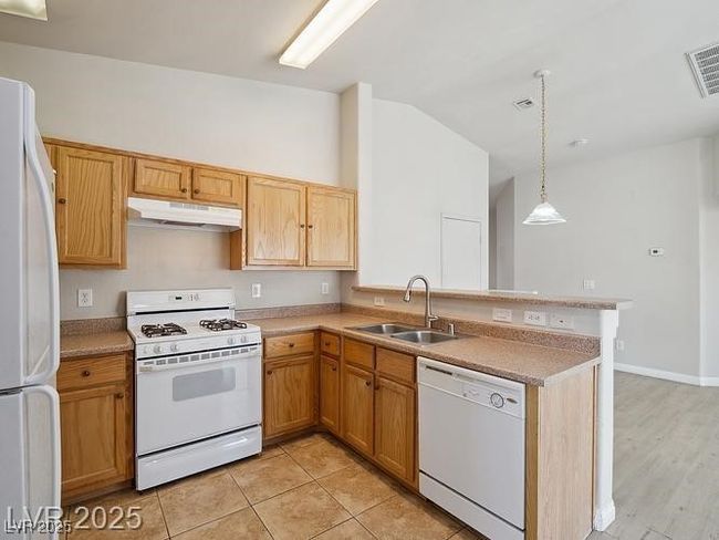 Kitchen featuring white appliances, a peninsula, light countertops, under cabinet range hood, and vaulted ceiling | Image 7