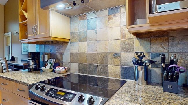 Kitchen with decorative backsplash, light stone countertops, stainless steel electric range oven, and exhaust hood | Image 8