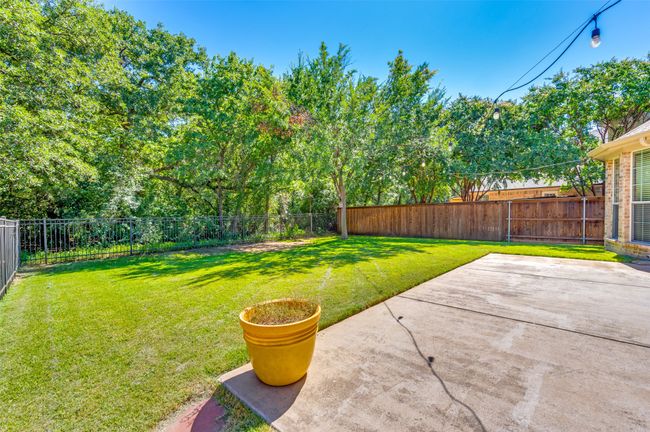 Fenced backyard featuring a patio area and greenspace behind. | Image 24