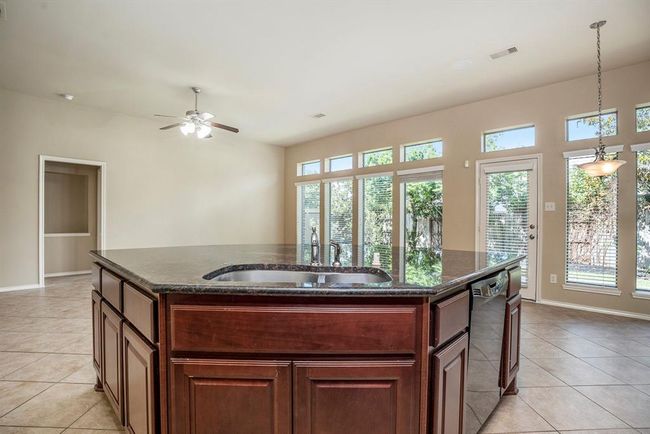 This bright and open kitchen is filled with natural light thanks to a wall of windows and a glass door leading to the backyard. Rich wood cabinetry, a tile backsplash, and a spacious curved island with granite countertops give the space warmth and function. | Image 14