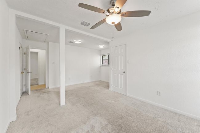 This room features neutral carpeting and walls, a ceiling fan with light, and a small window for natural light. It has a partition wall, creating a cozy layout, and access to an adjoining room or hallway. | Image 23