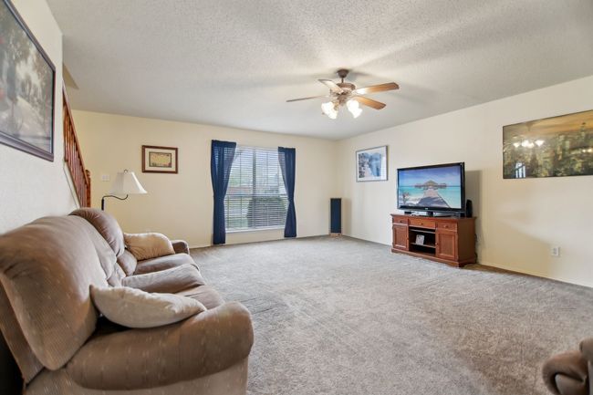 Carpeted living area featuring a textured ceiling, baseboards, and ceiling fan | Image 6
