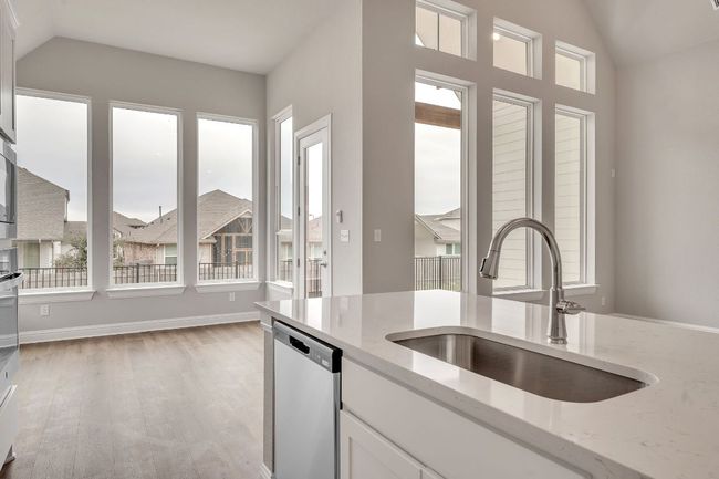 Kitchen featuring dishwasher, lofted ceiling, light stone countertops, white cabinetry, and a sink | Image 12