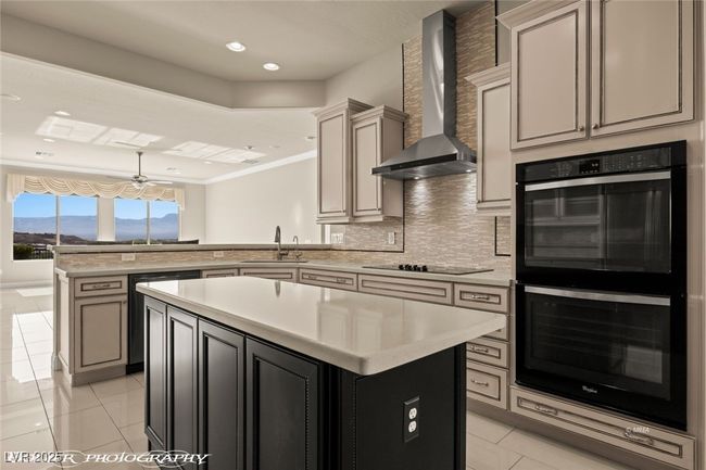 Kitchen with wall chimney range hood, a peninsula, light countertops, black appliances, and a sink | Image 15