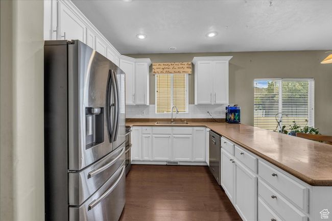 Kitchen featuring white cabinetry, a sink, stainless steel appliances, dark wood-style floors, and a peninsula | Image 8