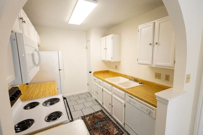 Kitchen featuring a sink, white appliances, arched walkways, light countertops, and a textured ceiling | Image 28