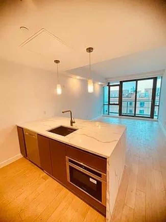 Kitchen with a sink, oven, light wood-type flooring, a peninsula, and light stone counters | Image 23