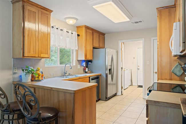 Kitchen featuring a sink, appliances with stainless steel finishes, a peninsula, backsplash, and light tile patterned floors | Image 22