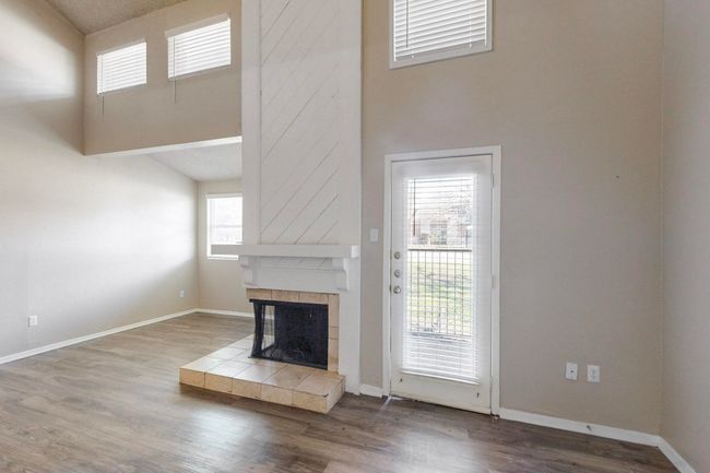 Unfurnished living room with a tiled fireplace, a high ceiling, wood finished floors, and baseboards | Image 12