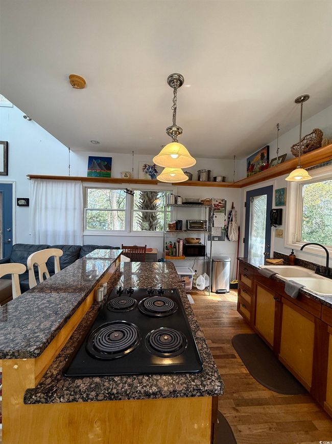 Kitchen featuring wood finished floors, hanging light fixtures, a sink, and black electric cooktop | Image 11