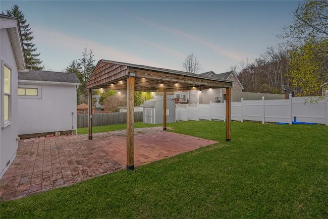Yard at dusk featuring a fenced backyard, an outdoor structure, a patio, and a storage shed | Image 21