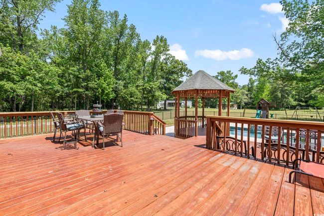 Wooden deck with a gazebo, outdoor dining area, a fenced backyard, and view of scattered trees | Image 23