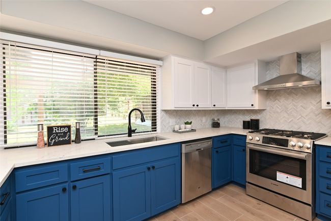 Kitchen featuring stainless steel appliances, wall chimney range hood, white cabinetry, backsplash, and light-wood style hard tile finished floors | Image 9
