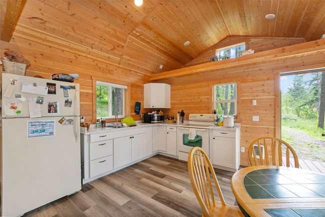Kitchen with white appliances, plenty of natural light, lofted ceiling, wood walls, and white cabinetry | Image 9