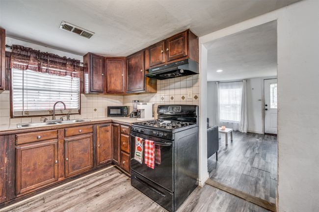 Kitchen with black appliances, under cabinet range hood, light wood-style floors, and backsplash | Image 8