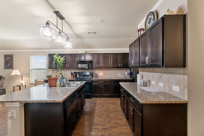 Kitchen with a sink, visible vents, dark brown cabinets, black appliances, and backsplash | Image 4