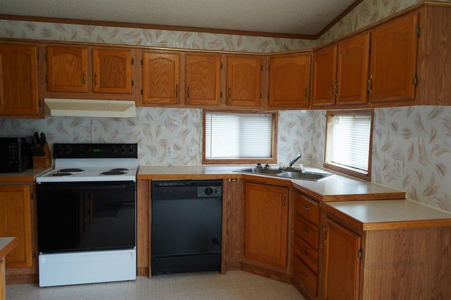Kitchen with black appliances, brown cabinetry, light flooring, under cabinet range hood, and light countertops | Image 10