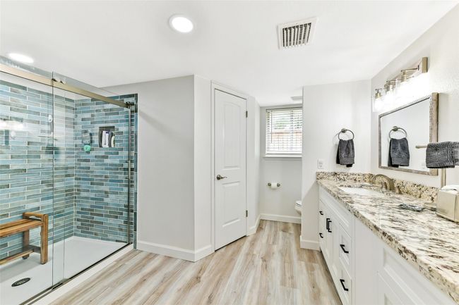 This modern bathroom features a spacious glass-enclosed shower with stylish blue tiling, a dual-sink vanity with granite countertops, bright and inviting with ample lighting and a window for natural light. | Image 15