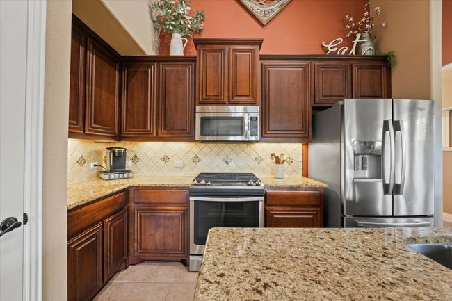 Kitchen featuring backsplash, light stone counters, stainless steel appliances, and light tile patterned flooring | Image 13