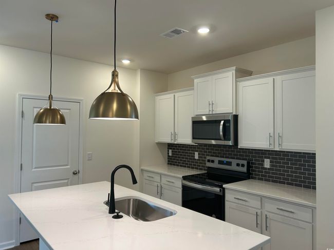 Kitchen featuring appliances with stainless steel finishes, a sink, decorative backsplash, white cabinetry, and an island with sink | Image 4