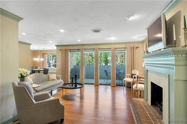 Living room with a notable chandelier, ornamental molding, a fireplace with raised hearth, visible vents, and wood finished floors | Image 12