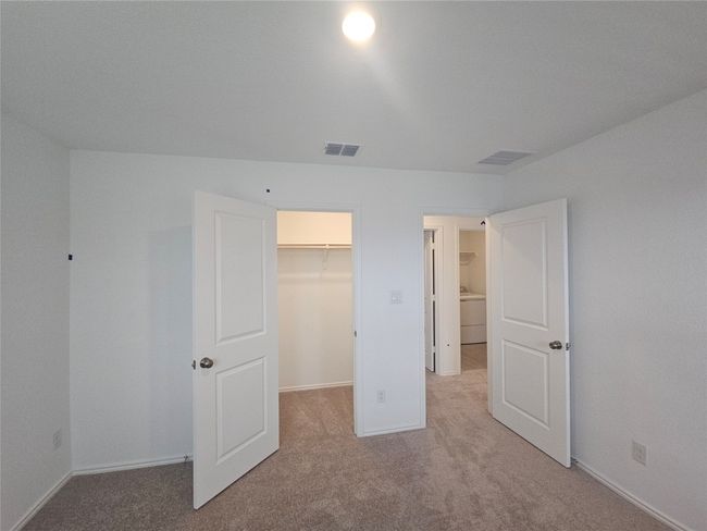 Unfurnished bedroom with washer / dryer, carpet flooring, a walk in closet, and baseboards | Image 11