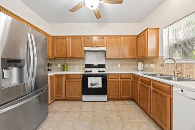 Kitchen featuring stainless steel fridge, dishwasher, range with gas stovetop, under cabinet range hood, and a ceiling fan | Image 10