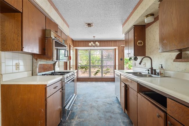 Kitchen with stainless steel appliances, a textured ceiling, light countertops, a chandelier, and brown cabinetry | Image 4