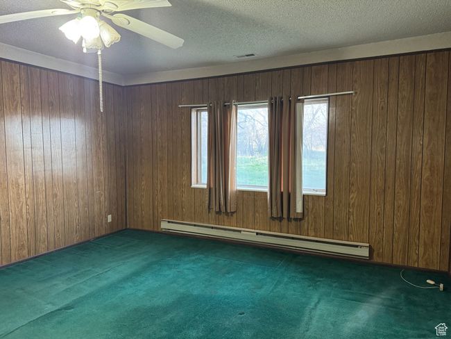 Carpeted empty room with a baseboard heating unit, wooden walls, ceiling fan, and a textured ceiling | Image 15