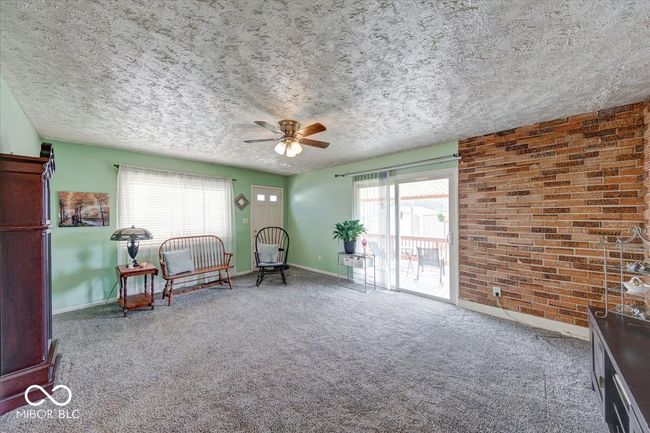 living area featuring baseboards, brick wall, ceiling fan, a textured ceiling, and carpet flooring | Image 20
