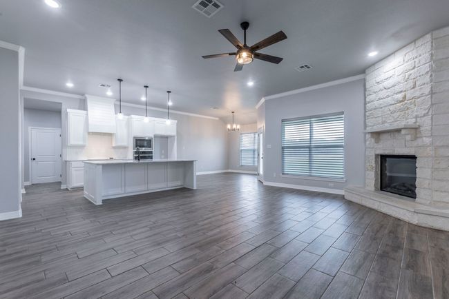 Unfurnished living room with a stone fireplace, a ceiling fan, crown molding, dark wood-style flooring, and a chandelier | Image 4