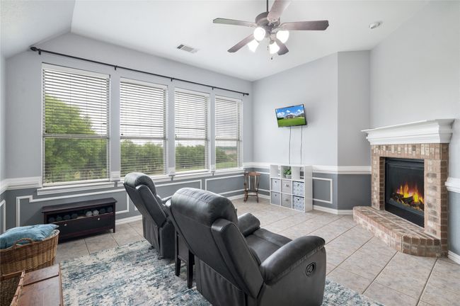 Tiled living area featuring a brick fireplace, a ceiling fan, vaulted ceiling, and a wainscoted wall | Image 6
