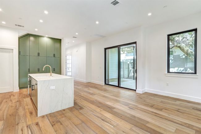 Kitchen with green cabinetry, a sink, light wood-type flooring, a kitchen island with sink, and baseboards | Image 25